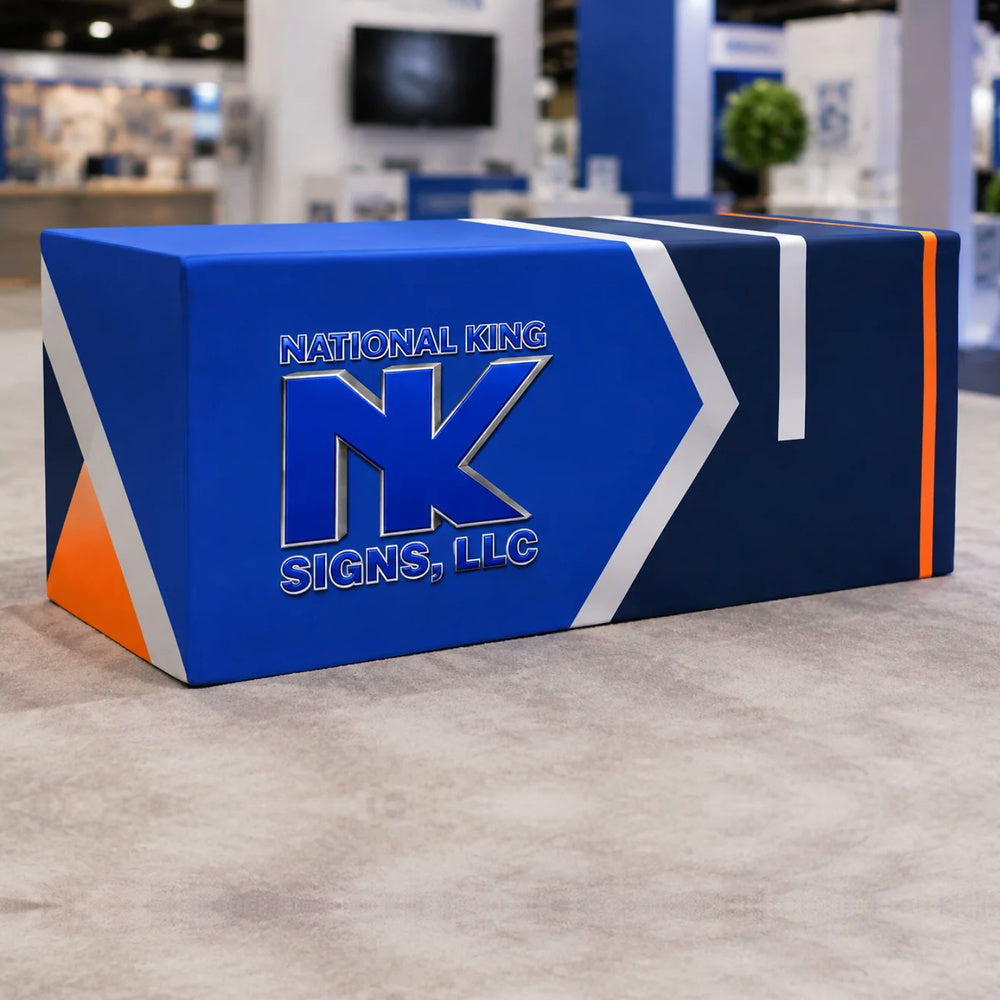 Print Solution Plus branded fitted table cover in royal blue and navy with white and orange accents, displayed at a trade show.